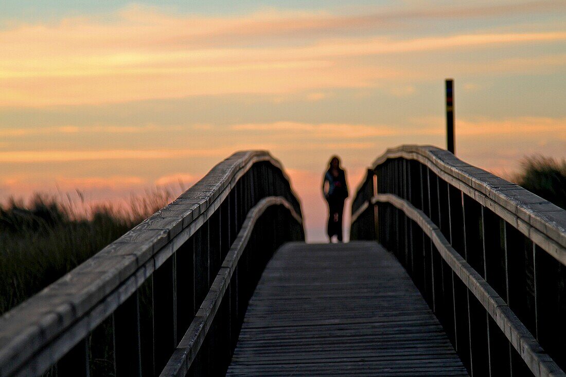 Woman a back light at wooden footbridge in sand dunes, Dunas del Espartal, Natural Park, Asturias, Spain