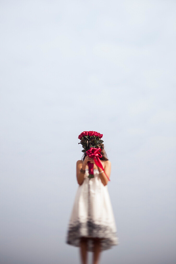 Young Woman Holding Bouquet of Red Roses in Front of Face