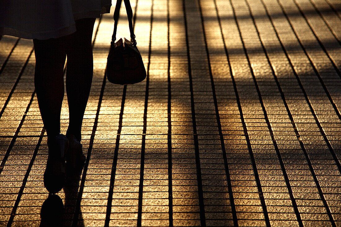 Frau in Stöckelschuhen mit Handtasche auf dem Bürgersteig, Nahaufnahme der Beine, Rückansicht Silhouette