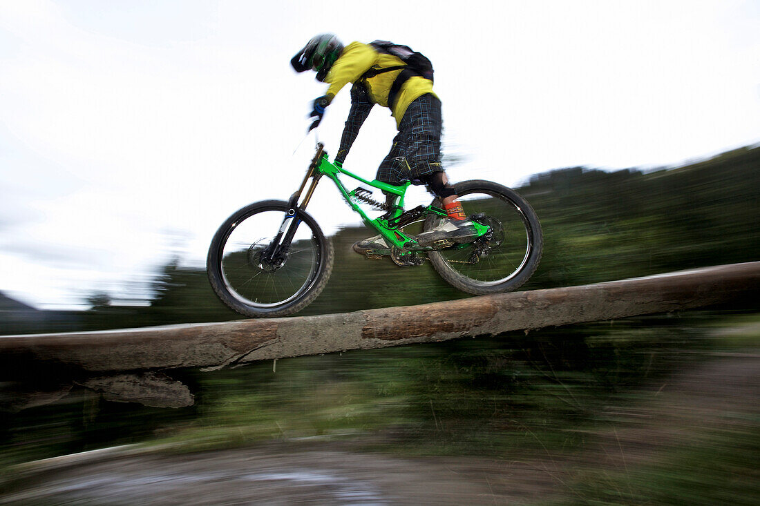 Freeride Mountainbiker fährt über einen Baumstamm, Chatel, Haute-Savoie, Frankreich