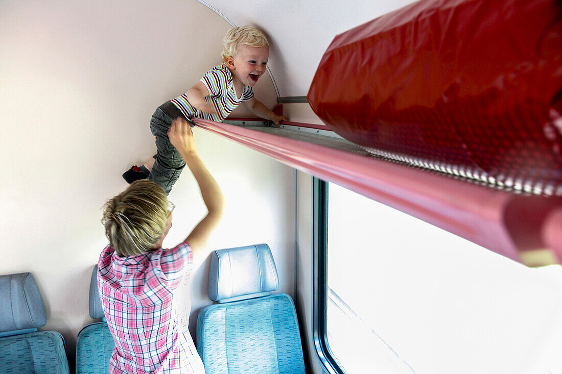 Junge (2 Jahre) klettert in die Gepäckablage in einem Zug, Insel Rügen, Mecklenburg-Vorpommern, Deutschland