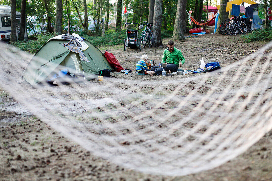 Family on a campsite, father and son cooking dinner, sitting on the ground, tent, hamock, Cycling trip of a family, summer, Baltic Sea, MR, beach near Bakenberg, Wittow Peninsula, Island of Ruegen, Mecklenburg West-Pomerania, Germany