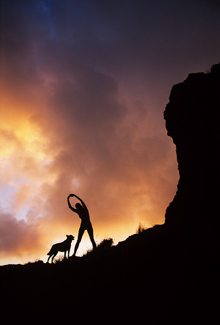 Hawaii, Silhouette of a woman stretching on a mountain top at sunset.