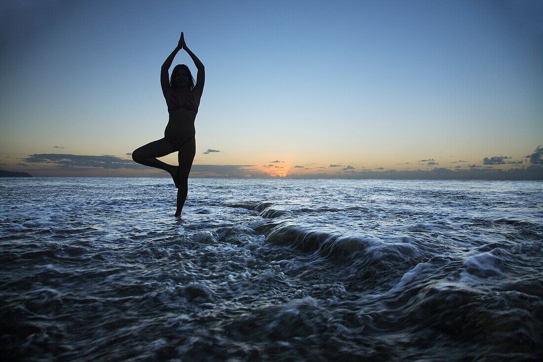 Hawaii, Oahu, Fit young girl on the beach doing yoga on the rocky coastline.