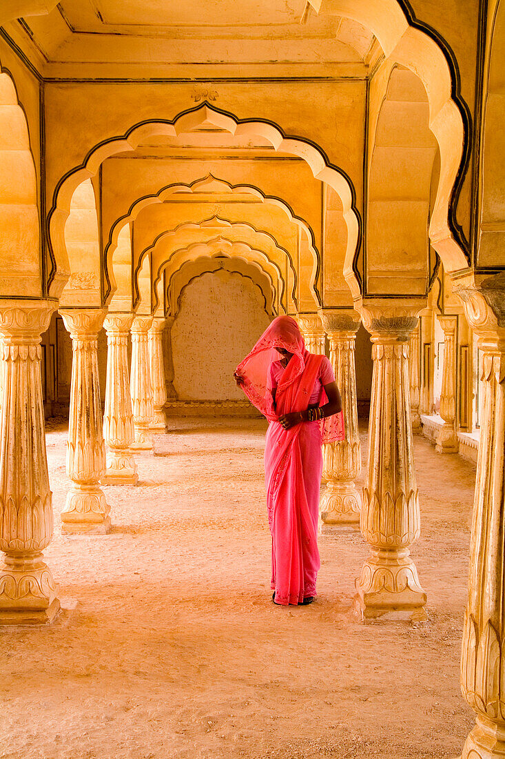 India, Rajasthan, Jaipur, Amber Fort Temple, woman in bright pink sari stands beneath arches.