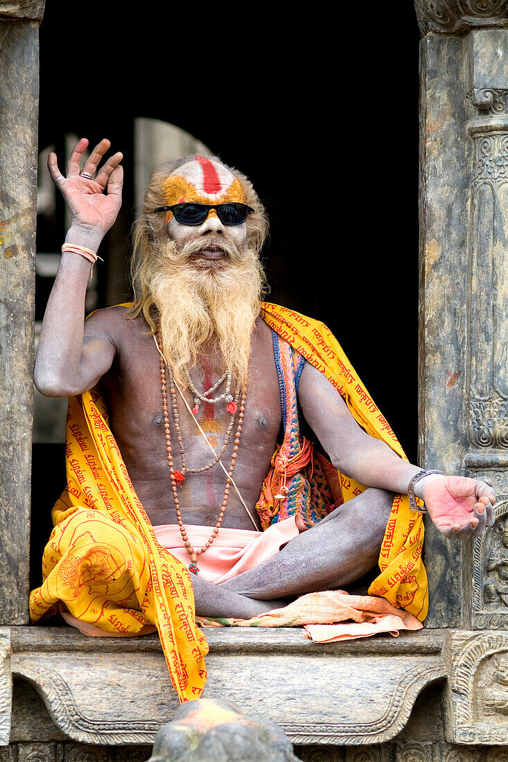 Nepal, Kathmandu, painted religious man wearing western sunglasses at Pashupatinath holy Hindu place on Bagmati River.