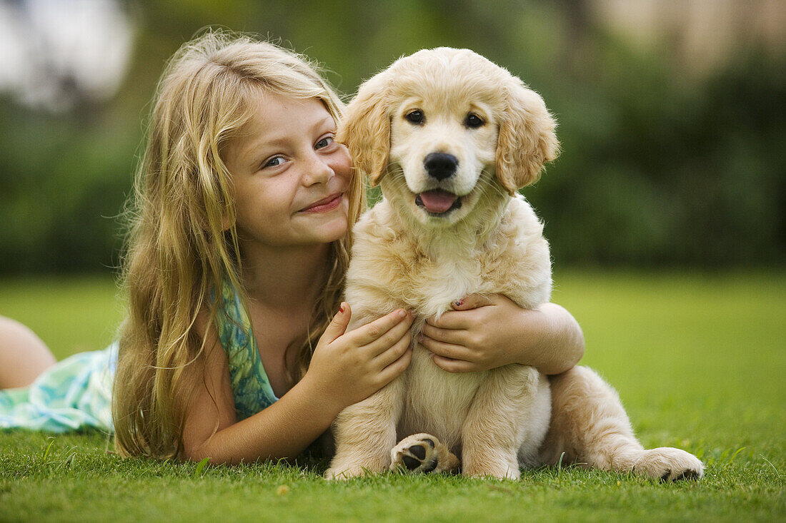 Hawaii, Maui, little girl sits on grass holding a golden retriever puppy.