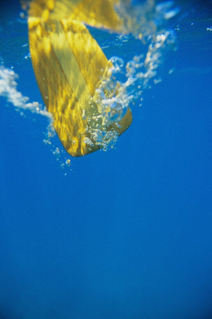 Underwater view of yellow paddle stroking water, creating bubbles.