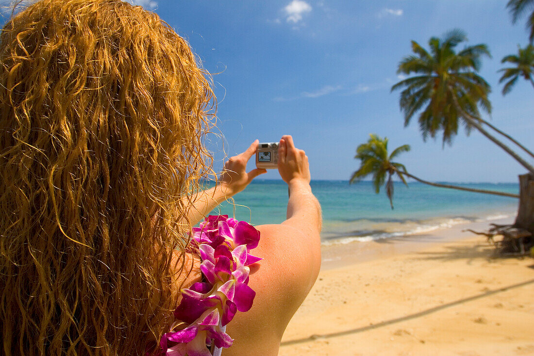 Hawaii, Oahu, Beautiful young woman photographing tropical beach with lei.