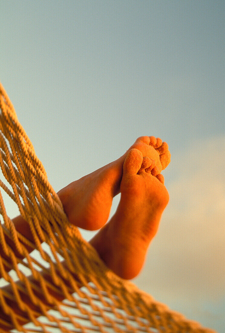 Close-up of bottom woman's feet crossed, hammock with golden afternoon light, sand