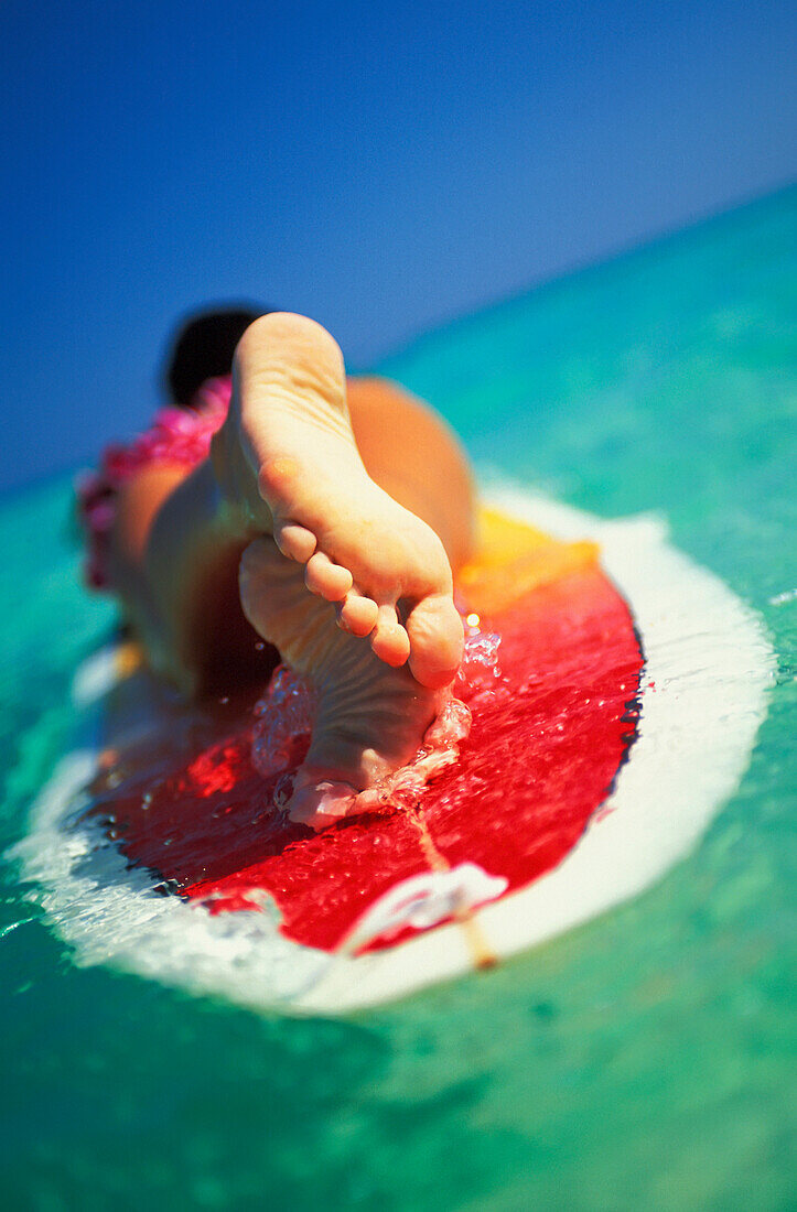 Hawaii, Oahu, Lanikai beach, close-up view from feet of woman with lei lying on surfboard
