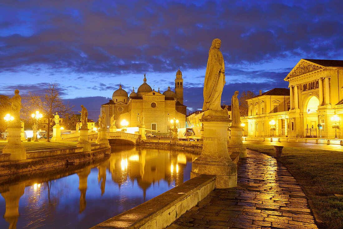 Statues along a  fcanal with San Giustina church in the background, illuminated, Prato della Valle, Padua, Veneto, Italy