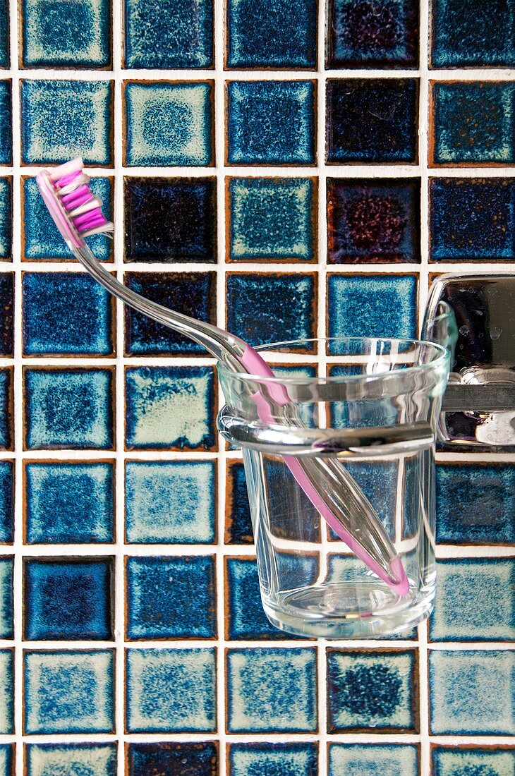 Zahnbürste in Glasbecher vor blauen Fliesen