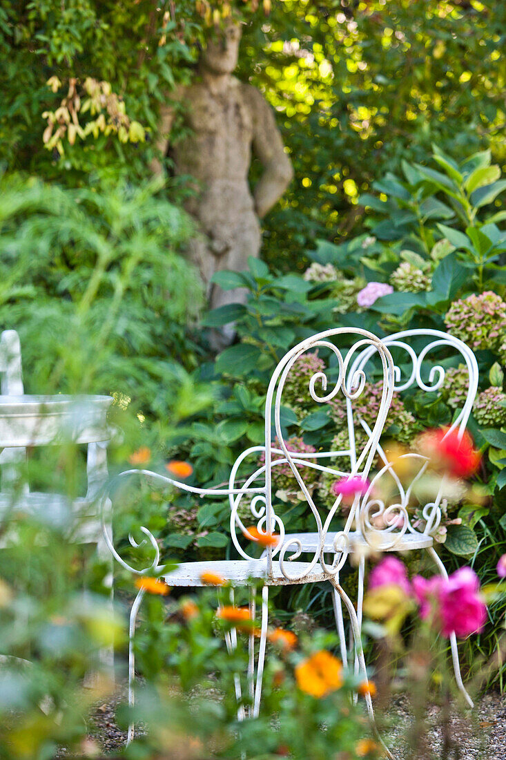 Weisse Stühle im bluhenden Garten mit Statue im Hintergrund, Wien, Österreich