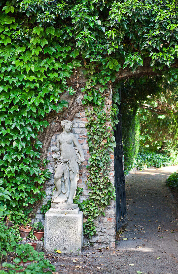 Statue at the entrance to the garden, fence overgrown with wild grape, Vienna, Austria