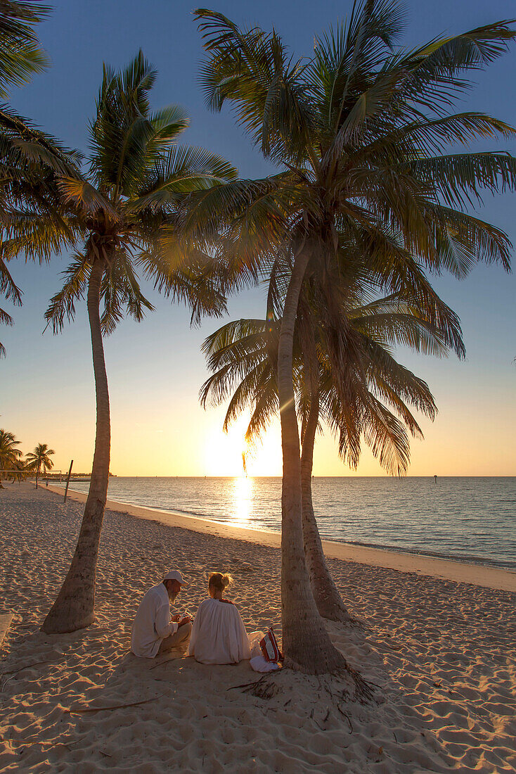 Couple sitting at sunrise on Key West Smathers Beach, Key West, Florida Keys, Florida, USA