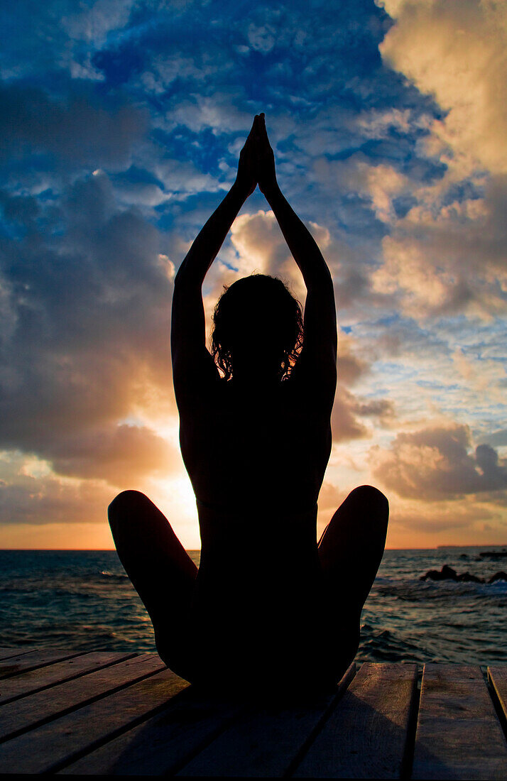 Silhouette of woman doing yoga on oceanside pier.