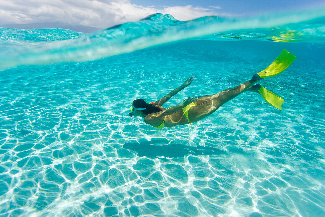 Woman snorkeling in tropical ocean water, Over/under view.