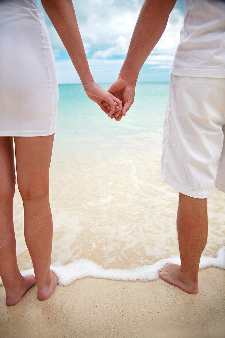 Hawaii, Oahu, Young engaged couple facing the beach holding hands, view from behind