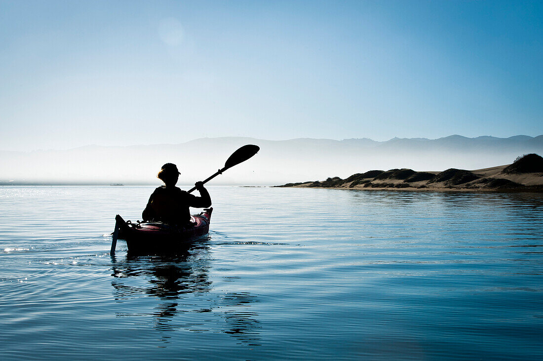 California, Morro Bay State Park, Woman kayaking in ocean, silhouette.