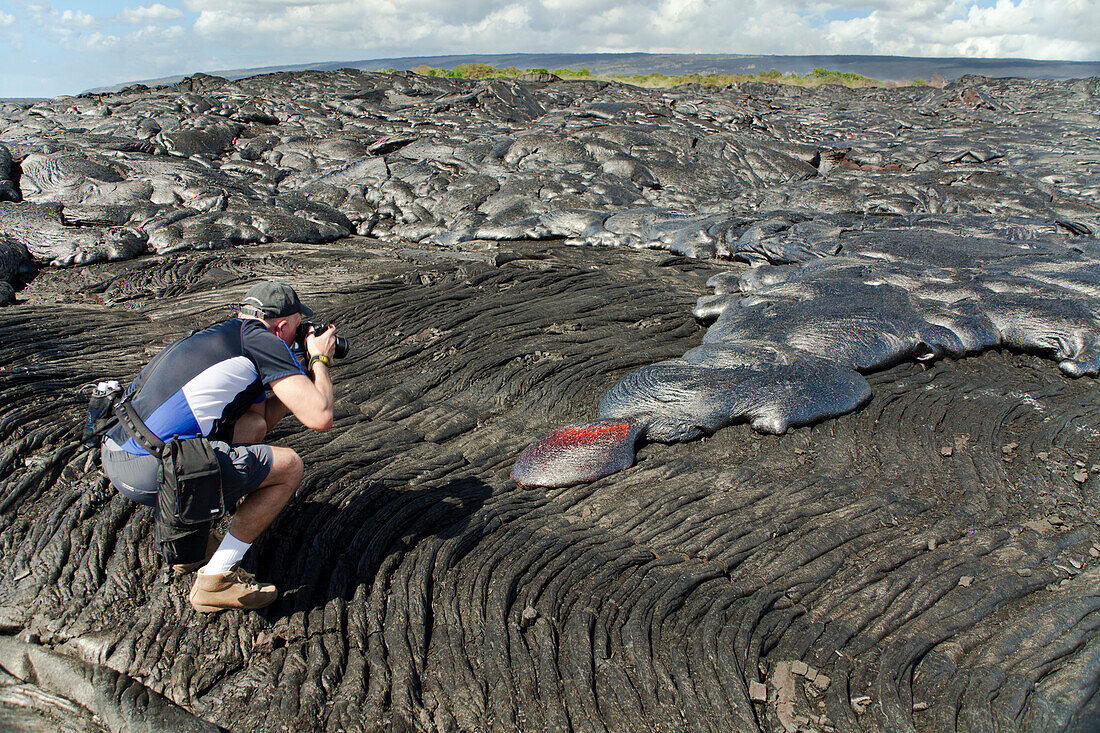 Hawaii, Big Island, Kalapana, Man photographs Pahoehoe lava flowing from Kilauea covering an older Pahoehoe flow.