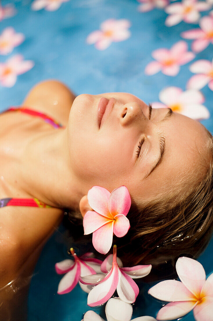 Hawaii, Oahu, Young girl resting in a pool with plumerias.