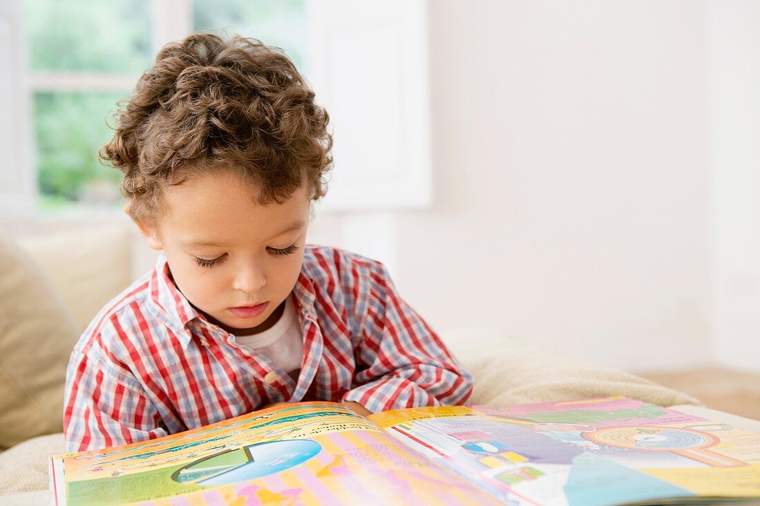 Vierjähriger Junge liest ein Buch auf dem Sofa