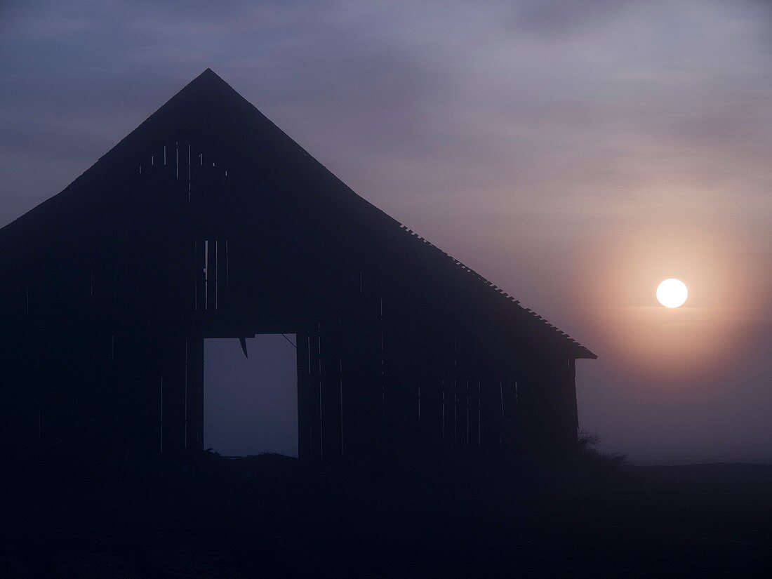 The sun rises in the open doorway of a barn in Corcoran, California, United States