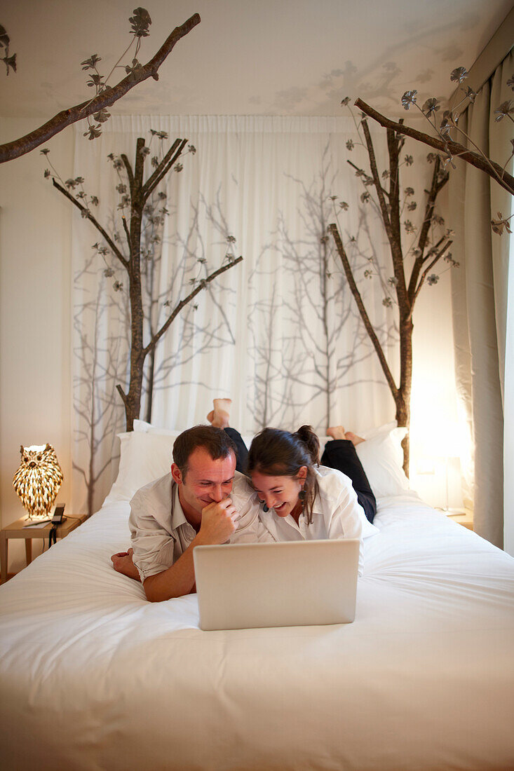 Junges Paar liegt mit einem Laptop auf einem Bett, Hotel Maison Moschino, Mailand, Lombardei, Italien