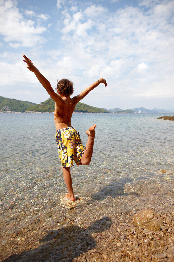 Boy in crane pose in shallow waters, bay near Hotel Sipan, Sipanska Luka, Sipan island, Elaphiti Islands, northwest of Dubrovnik, Croatia