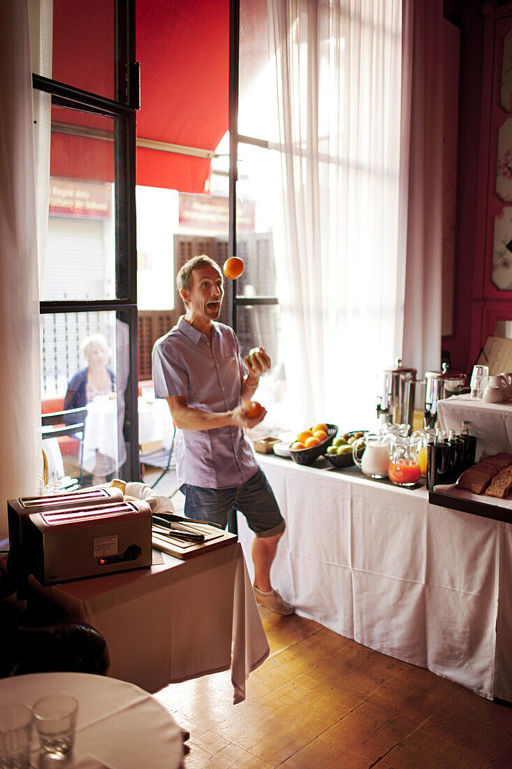 Man juggling with fruits inside a hotel breakfast room, Barcelona, Catalonia, Spain