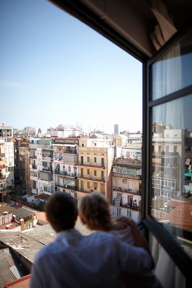 Couple enjoying the view out of a window of a hotel room, Barcelona, Catalonia, Spain