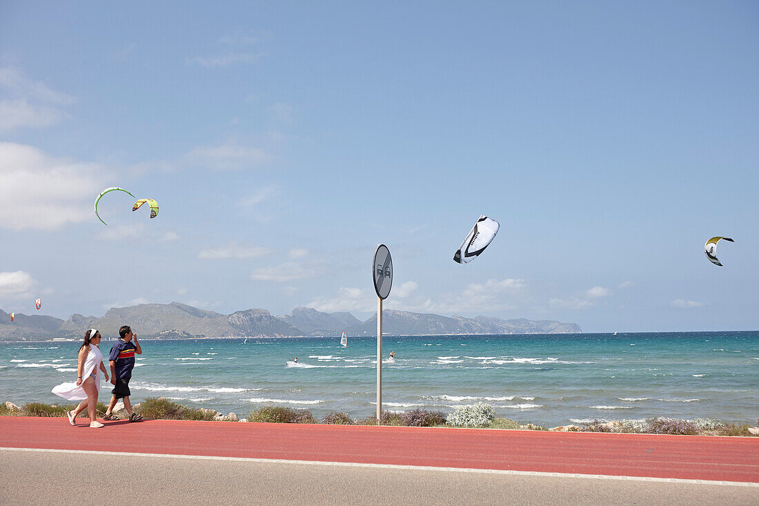 Touristen auf Fahrradweg, Kitesurfer an Küstenstraße am Club Pollentia, Bucht Badia de Pollenca, bei Alcudia, Mallorca, Balearen, Spanien