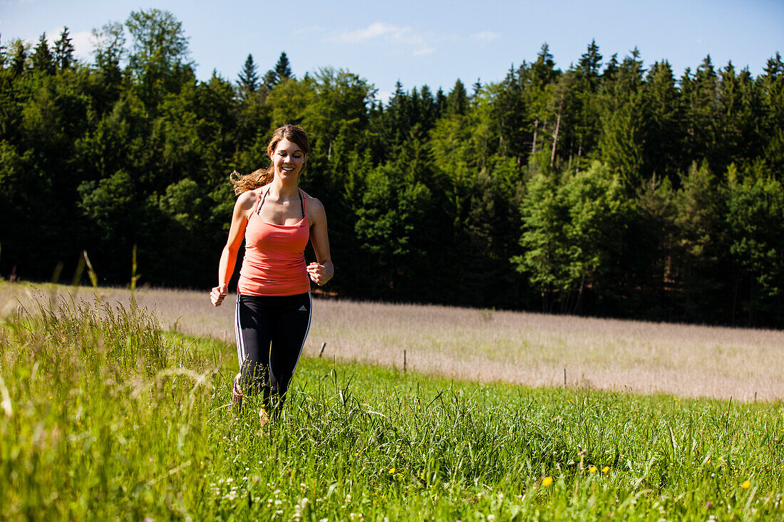 Young woman jogging over a meadow, Upper Bavaria, Germany