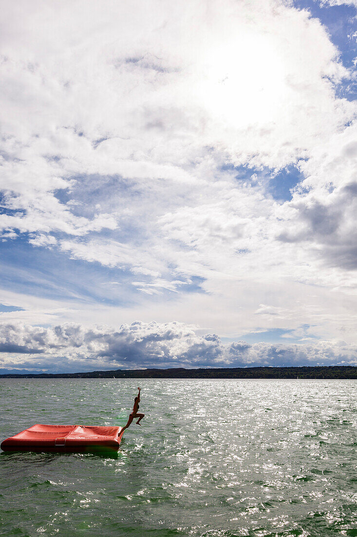 Young woman jumping from a floatable platform into Lake Starnberg, Bavaria, Germany