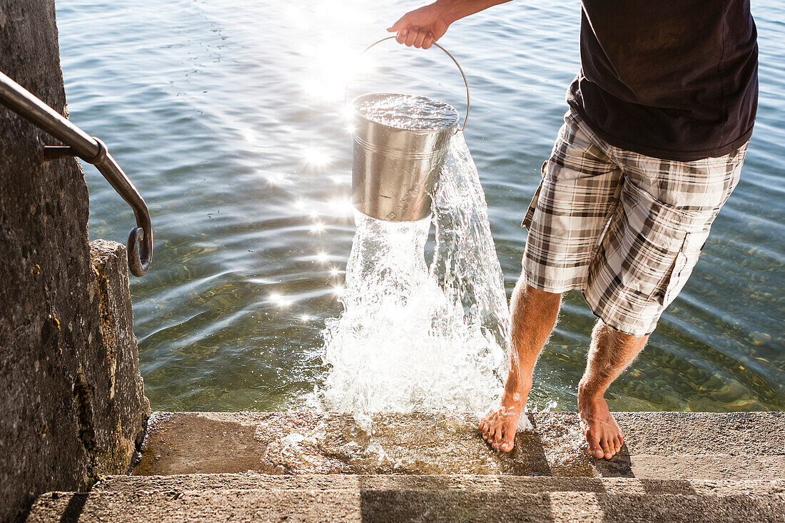 Mann schöpft mit Eimer Wasser aus dem Starnberger See, Bayern, Deutschland