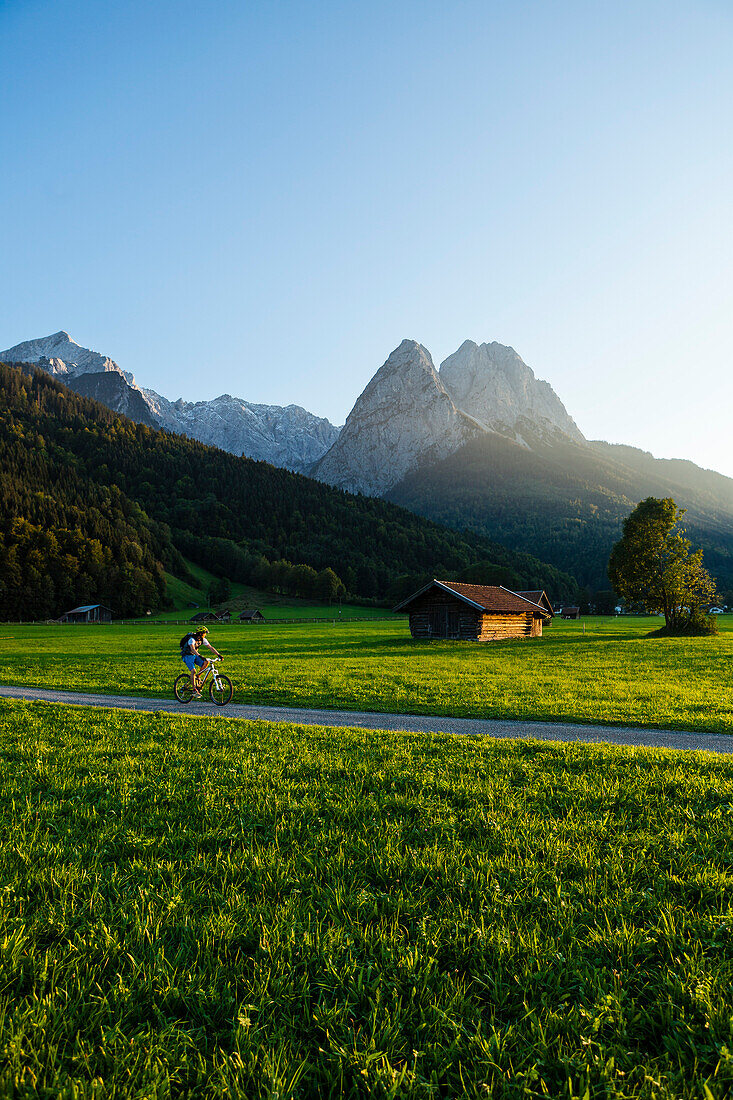 Mountainbiker fährt an Wiesen mit Heustadel vorbei, Grainau, Bayern, Deutschland