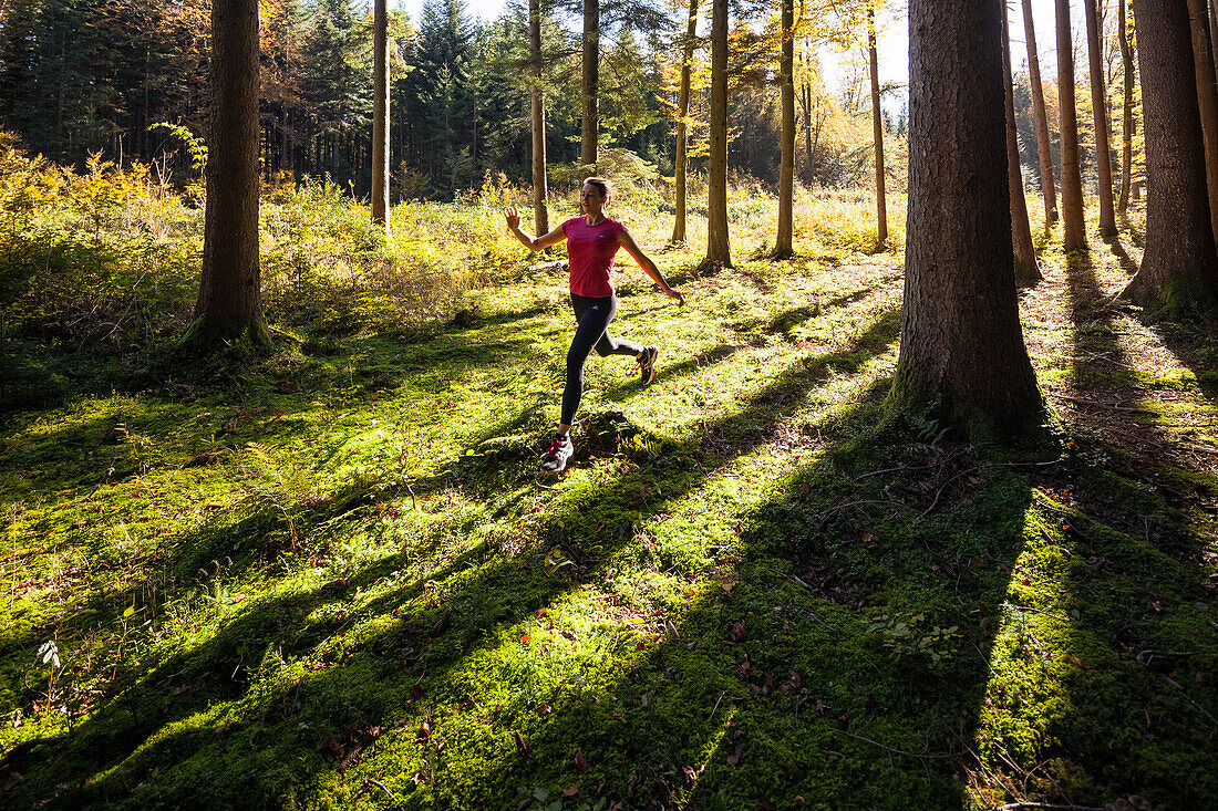 Young woman jogging through wood in autumn, Bavaria, Germany