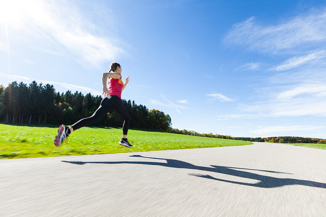 Woman jogging along a road, Munsing, Bavaria, Germany