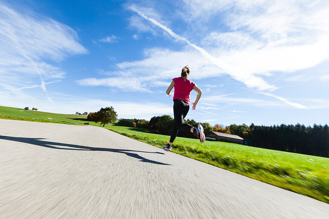 Joggerin läuft über Landstraße, Münsing, Bayern, Deutschland