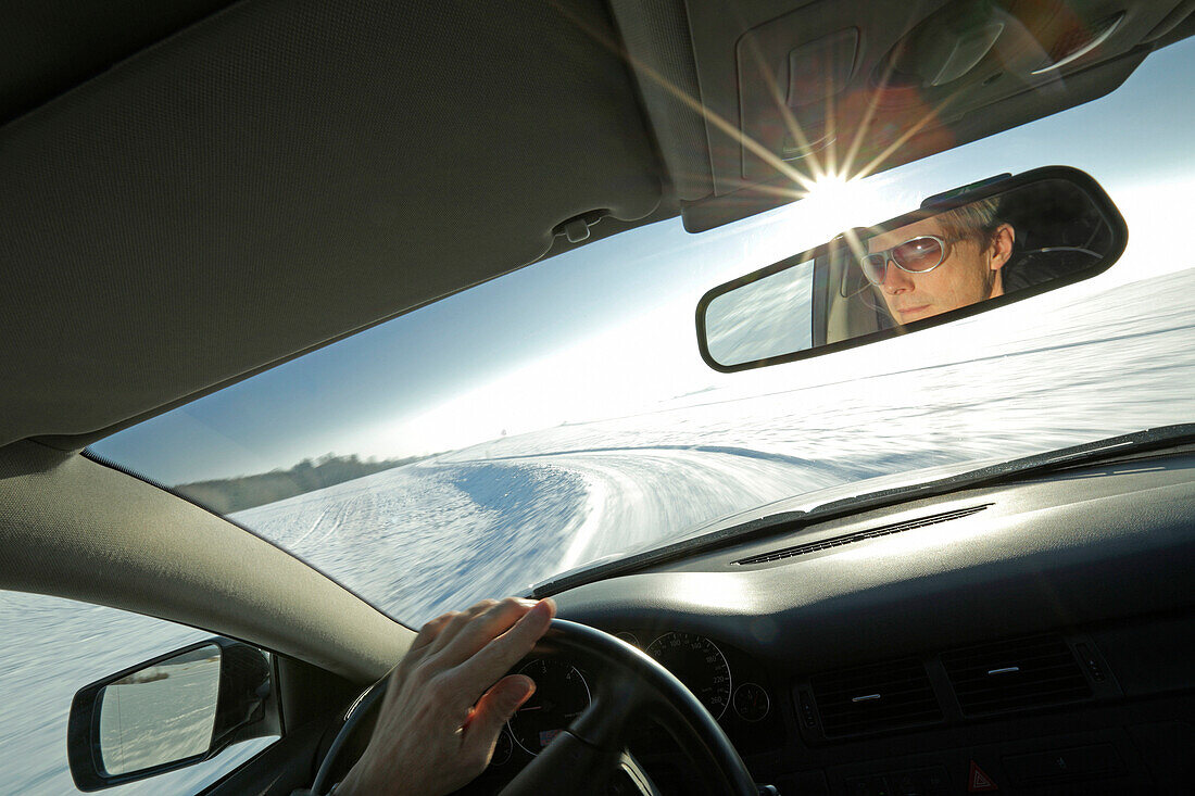 Man driving a car along a snow-covered street, Bavaria, Germany