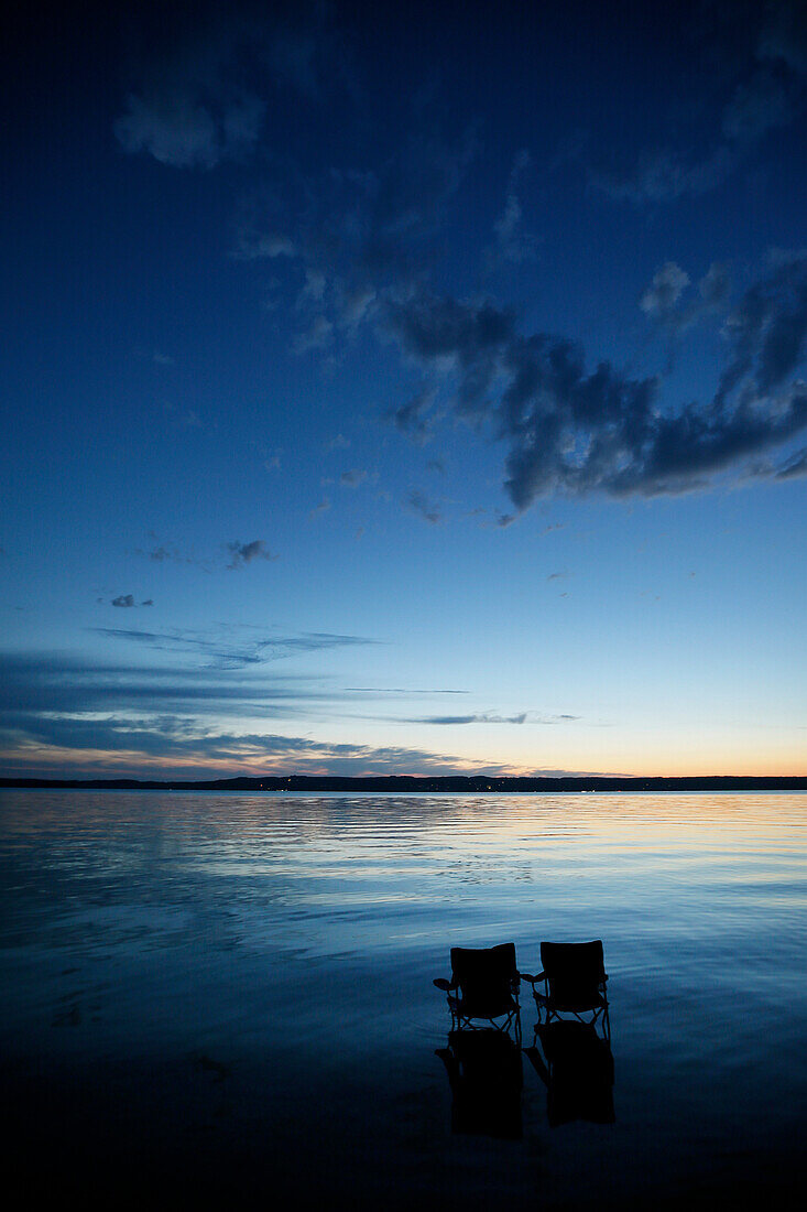 Two folding chairs in lake Starnberg in twilight, Bavaria, Germany
