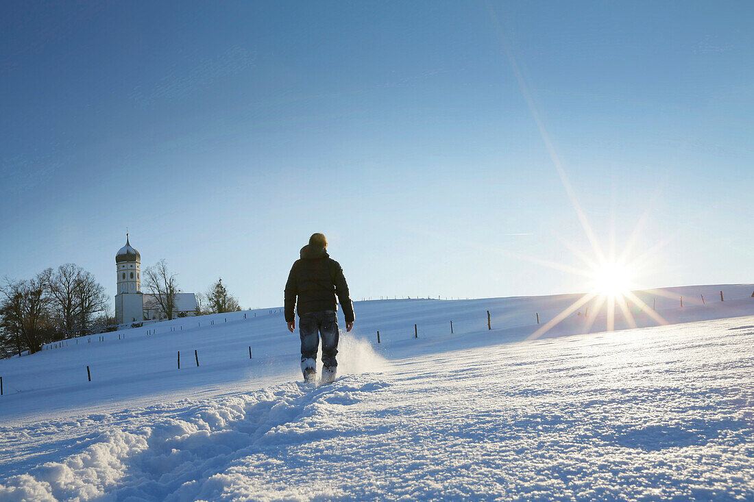 Man hiking through snow to Parish Church of St. John the Baptist, Holzhausen, Munsing, Bavaria, Germany