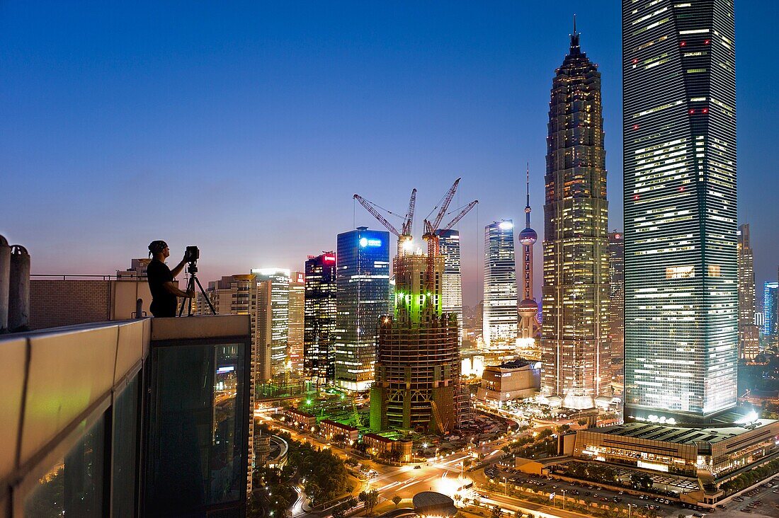 A photographer sets up his shot of Jin Mao Tower, the Shanghai World Financial Center and a building under construction