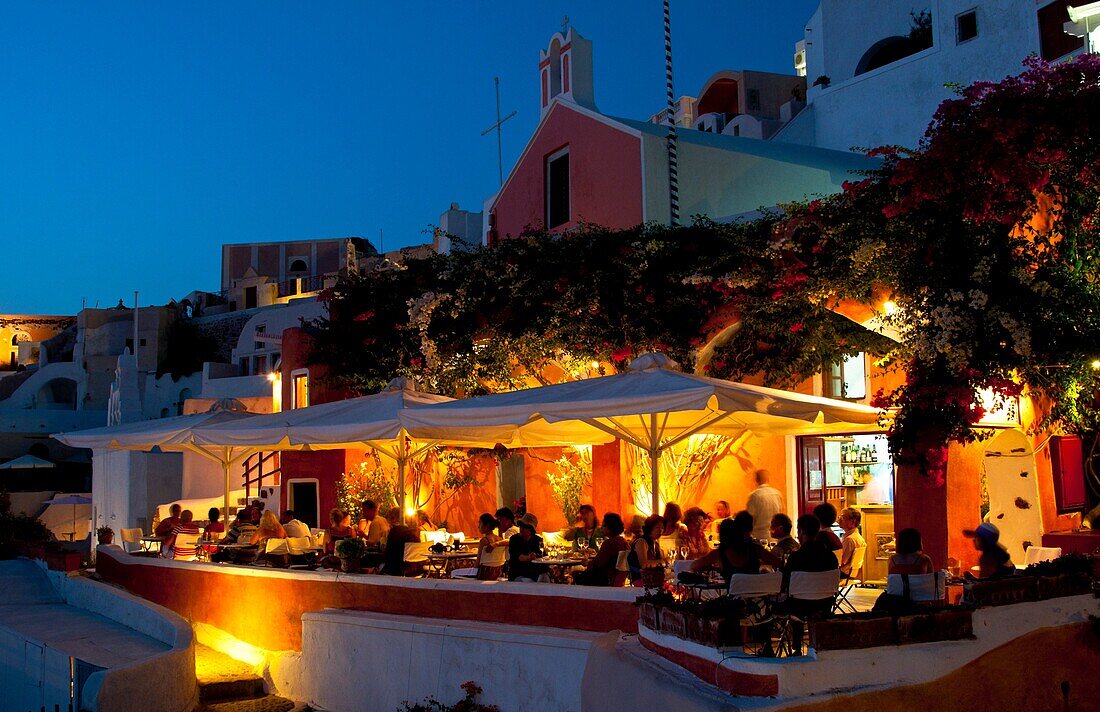 Night exposure after sunset of warm restaurant with tourists on cliff of beautiful Oia in Santorini Greece in Greek Islands