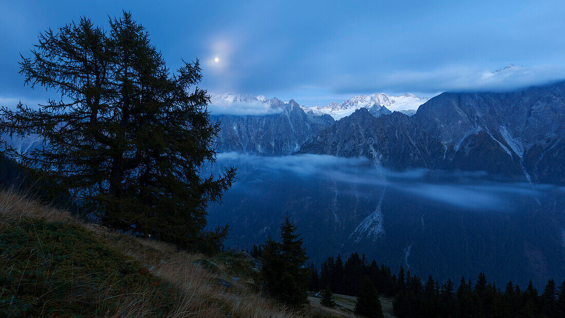 Vollmondnacht über dem tiefeingeschnittenen Bergell-Tal mit Nebel in verschiedenen Höhenlagen, Engadin, Schweiz