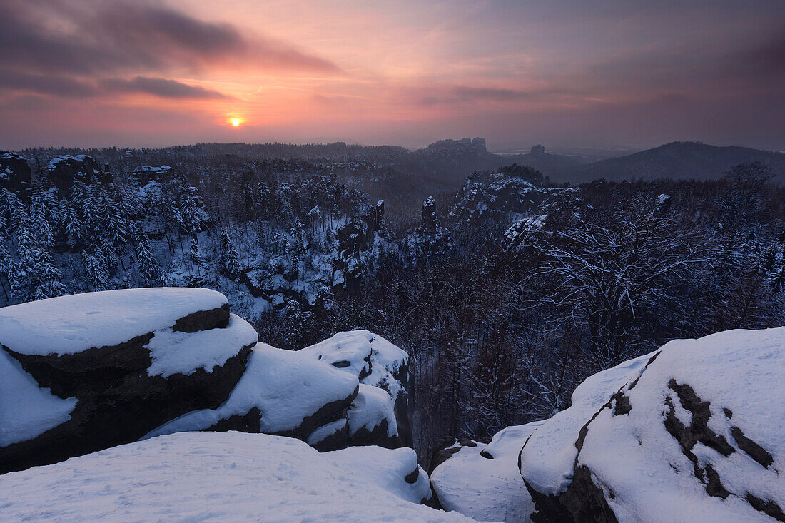 Sunset above the Saxon Switzerland national park with a wide view from Carolafelsen above the heavily snow covered landscape, Saxony, Germany