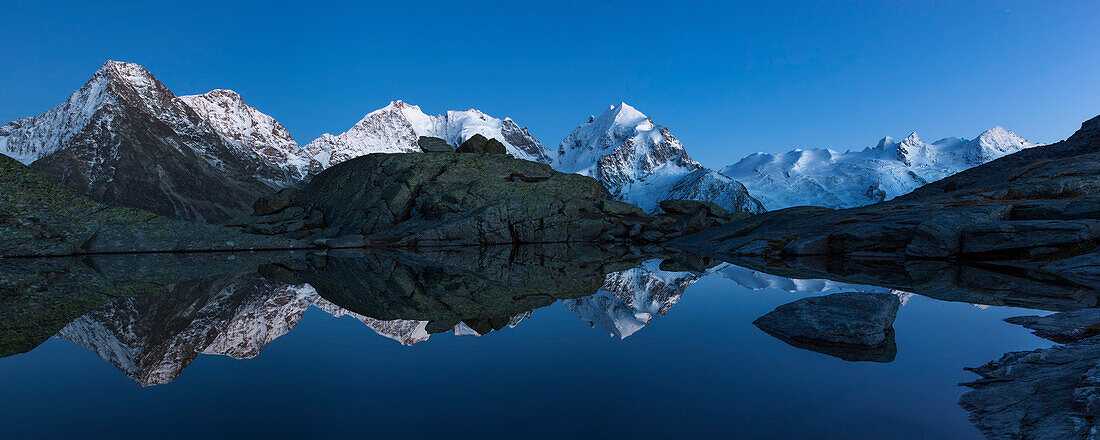 Perfekte Spiegelung der Bernina-Roseg-Gruppe in einem kleinen Bergsee nahe der Hütte Fuorcla Surlej im Blau der Dämmerung, Engadin, Schweiz