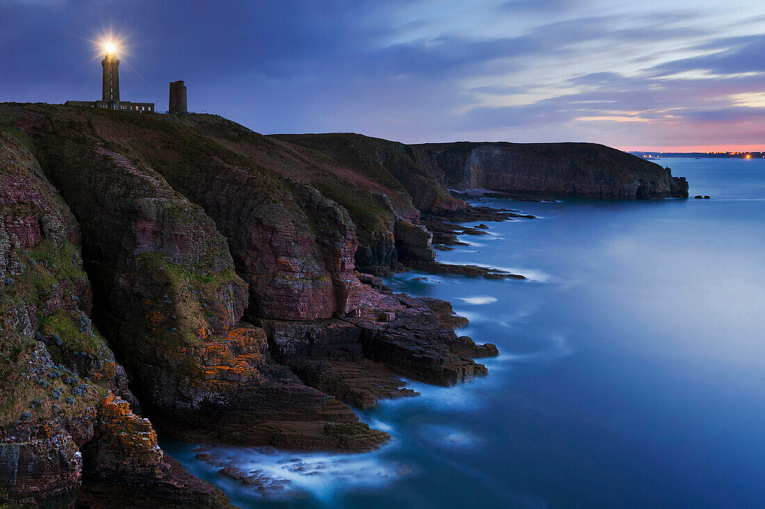 Cap Frehel lighthouse at the top of the 70-meter high cliffs in north-west France in blue light at dusk, Brittany, France