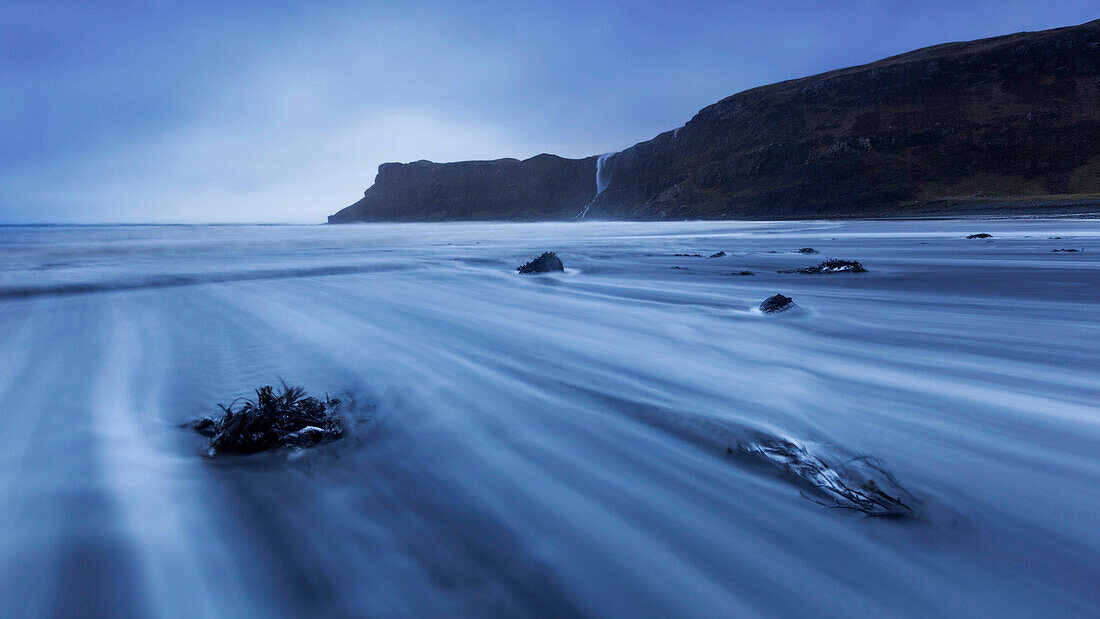 Langzeitbelichtung am Strand von Talisker im Blau der Dämmerung mit Blick auf die imposanten Klippen auf der Isle of Skye, Schottland, Großbritannien